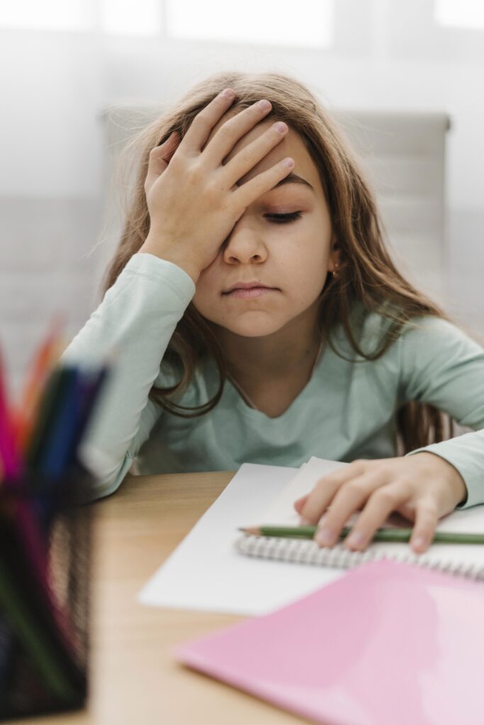 blonde little girl having headache while doing online classes