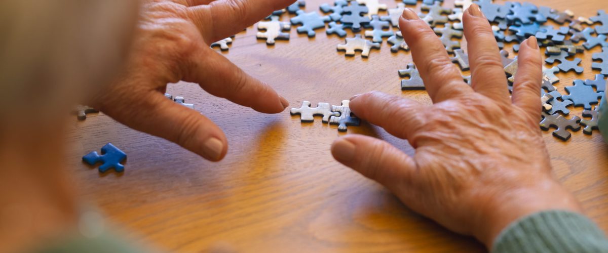 hands of caucasian senior woman playing with jigsaw puzzles in sunny dining room at home. retirement, wellbeing, activities, togetherness and senior lifestyle, unaltered.